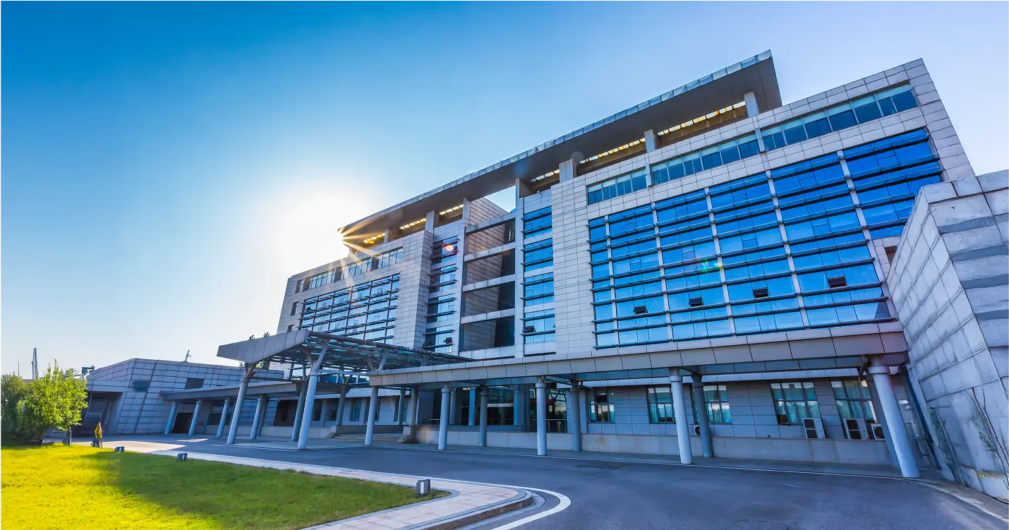 A modern multi-story building featuring extensive glass windows and a covered entrance that stands tall. The sleek architectural design mirrors the sophistication seen in JAECOO SUV HQ Office in China.